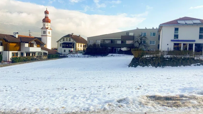 Schneebedecktes Grundstück in einer Wohngegend mit Blick auf umliegende Häuser und einen Kirchturm.