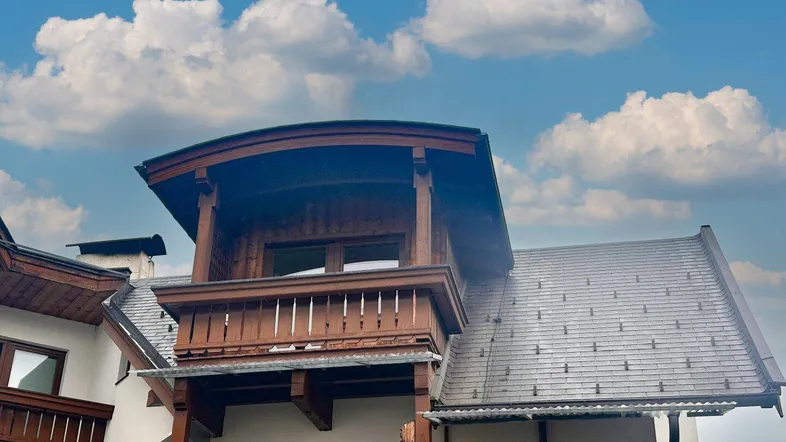 Detailansicht des Gebäudes mit traditionellem Holzbalkon und Dachkonstruktion unter blauem Himmel.