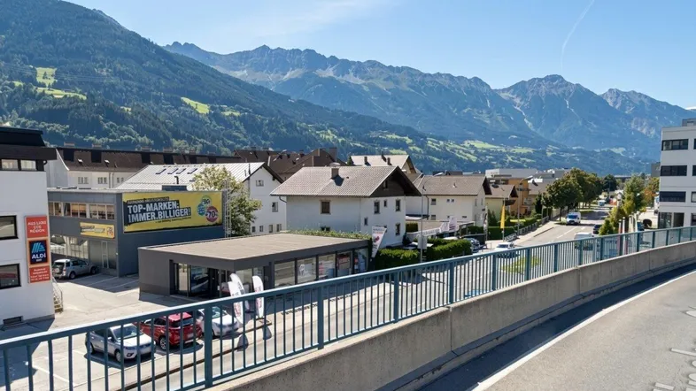 Blick auf ein modernes Geschäftsgebäude mit großen Glasfronten, umgeben von Bergen und einer Straße.