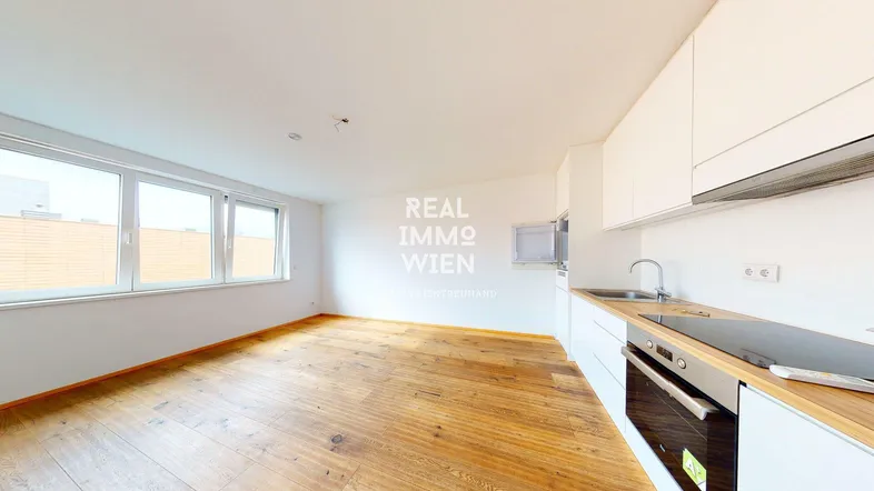 Helles, offenes Zimmer mit integrierter Küche, Holzboden und großen Fenstern für viel Tageslicht.