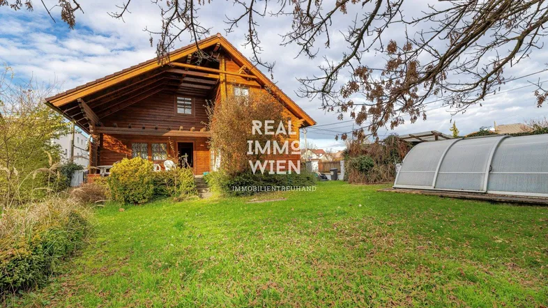 Charmantes Holzhaus mit großem Garten und viel Grünfläche unter bewölktem Himmel.