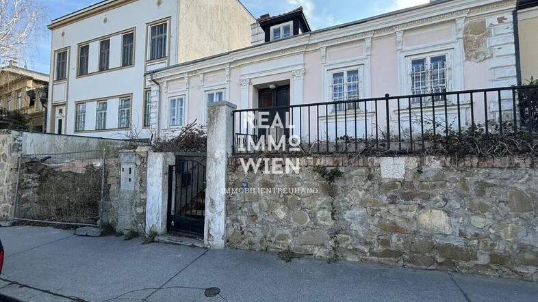 Historisches Gebäude mit steinerner Mauer und schmiedeeisernem Tor von der Straße aus gesehen.