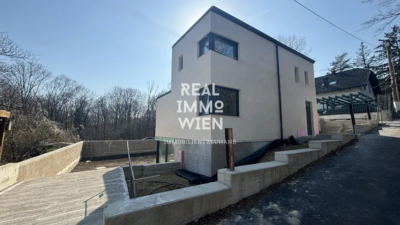 Moderne Neubauvilla mit klaren Linien und großen Fenstern, umgeben von Natur und sonnigem Ausblick.