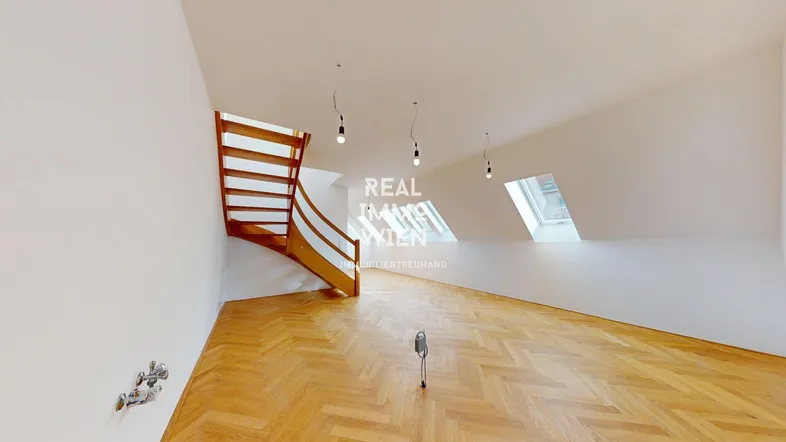 Helles Dachgeschosszimmer mit Fischgrätparkett, Dachschrägen und einer eleganten Holztreppe, die in die obere Etage führt.