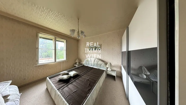 Schlafzimmer mit Teppichboden, großem Kleiderschrank und Fenster mit Blick ins Grüne.