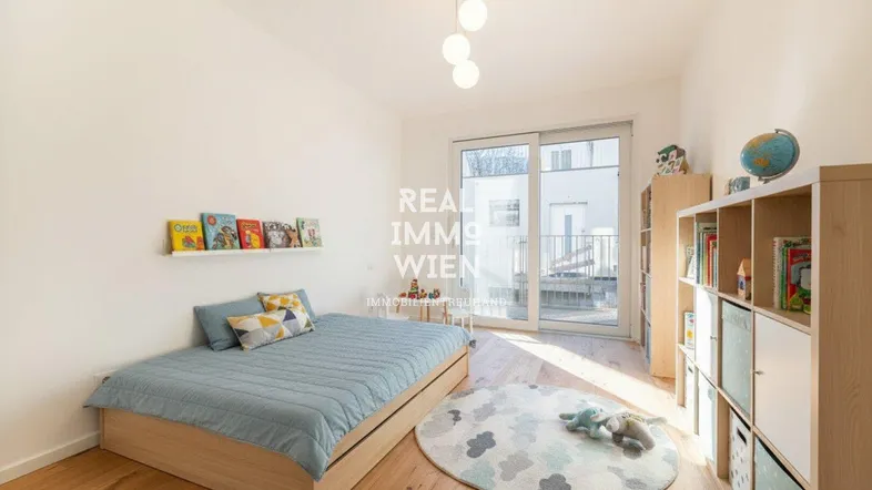 Helles Kinderzimmer mit Holzboden, Bett und Zugang zu einem kleinen Balkon.