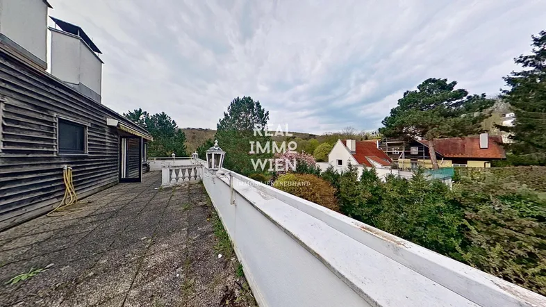Geräumige Terrasse mit Blick auf die umliegende grüne Landschaft und weitere Gebäude.