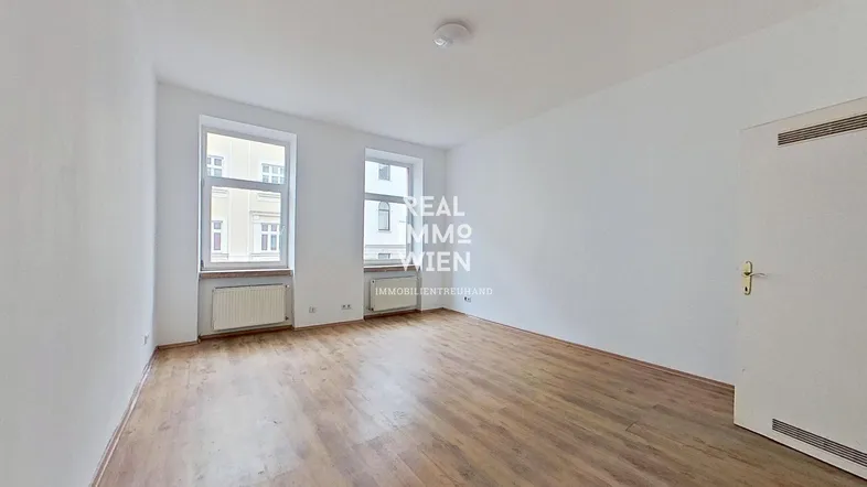 Helles, leeres Zimmer mit Holzfußboden und zwei Fenstern, bereit zur individuellen Gestaltung.
