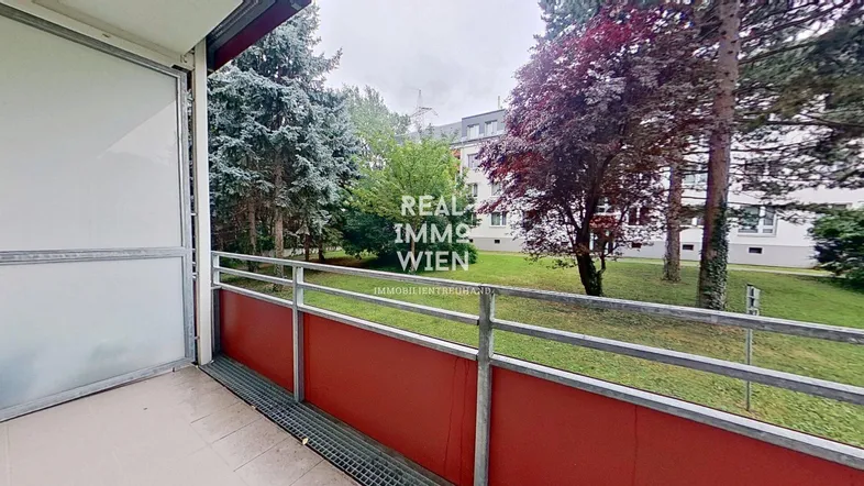 Balkon mit rotem Geländer und Blick ins Grüne sowie auf umliegende Gebäude.