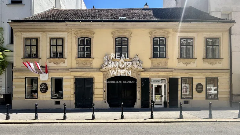 Historisches Gebäude mit gelber Fassade und klassischer Architektur, beherbergt ein Immobilienbüro im Erdgeschoss.