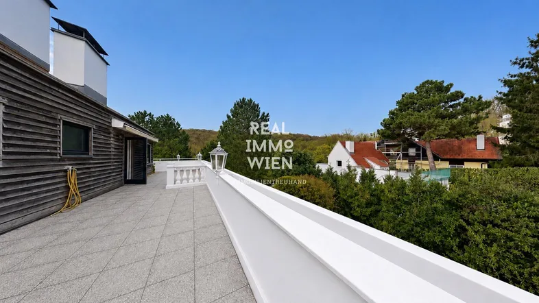 Geräumige Dachterrasse mit Fliesenboden, weißem Geländer und weitem Blick ins Grüne.