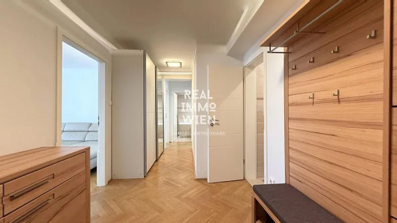 Heller Flur mit Holzparkettboden, Garderobe und integrierten Schränken, der zu weiteren Räumen führt.