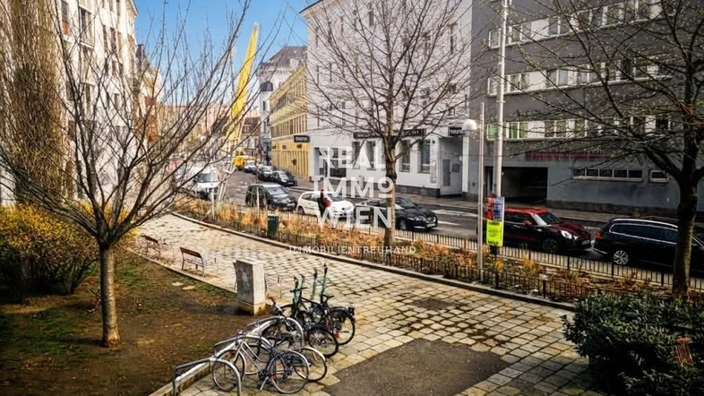Blick auf die belebte Straße mit parkenden Autos und Fahrrädern vor den umliegenden Gebäuden.