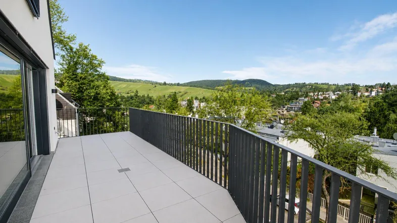Geräumiger Balkon mit Fliesenboden und weitem Blick über die grüne Hügellandschaft.