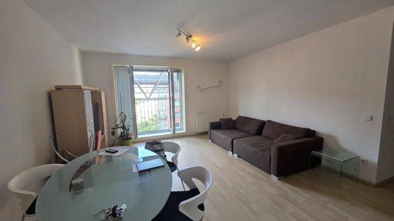 Heller Wohn- und Essbereich mit Parkettboden, großem Fenster und Zugang zu einem Balkon.