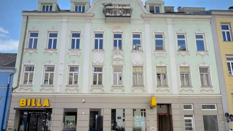 Historisches Gebäude mit mintgrüner Fassade, Stuckverzierungen und einem Geschäftslokal im Erdgeschoss.