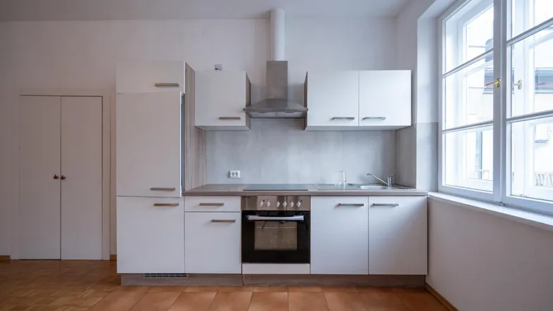 Funktionale Küche mit weißen Schränken, integrierten Geräten und einem Fenster für Tageslicht.