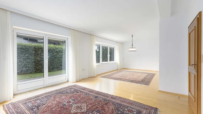 Helles Wohnzimmer mit Parkettboden, großen Fenstern und Zugang zum Gartenbereich.