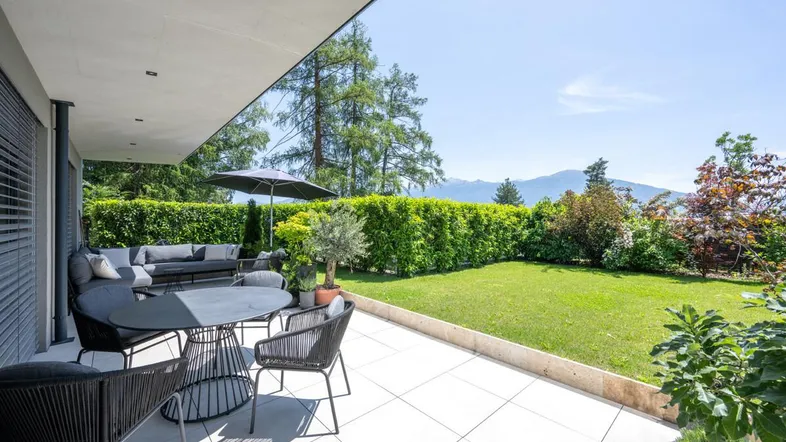 Geräumige Terrasse mit modernen Gartenmöbeln, umgeben von einem gepflegten Rasen und Hecken.