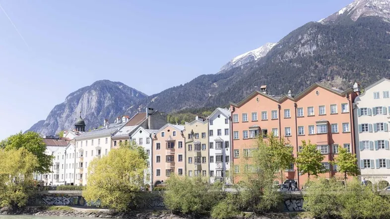 Blick auf die bunte Häuserzeile entlang des Flusses mit schneebedeckten Bergen im Hintergrund.