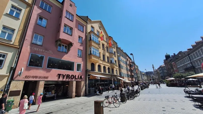 Belebte Einkaufsstraße mit historischen Gebäuden und Geschäften unter blauem Himmel.