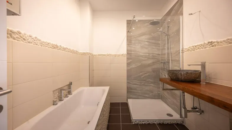 Modernes Badezimmer mit Badewanne, begehbarer Dusche und stilvollem Waschbecken auf Holzplatte.