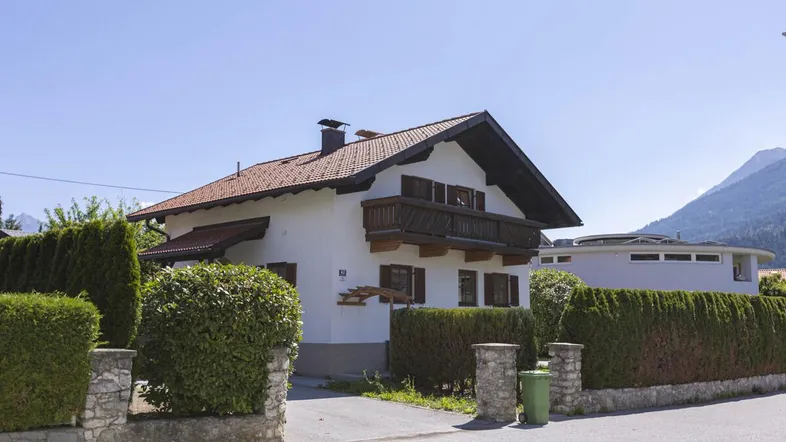 Traditionelles Haus im alpenländischen Stil mit Satteldach, Balkon und gepflegter Hecke im Vorgarten.
