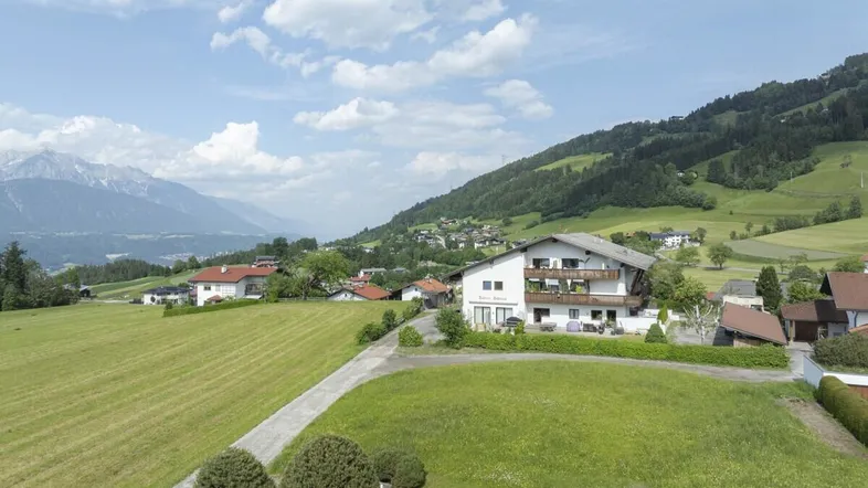 Panoramablick auf ein Wohngebäude in ländlicher Umgebung mit grünen Wiesen und Bergen im Hintergrund.