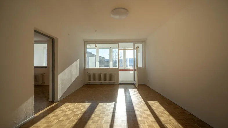 Helles Zimmer mit Parkettboden und großen Fenstern, das viel Sonnenlicht hereinlässt.