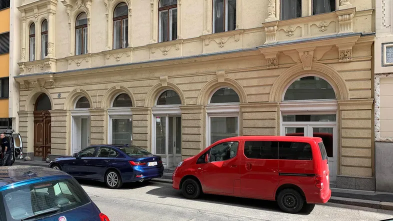 Historische Fassade eines Altbaus mit reich verzierten Details und großen Rundbogenfenstern an einer belebten Straße.