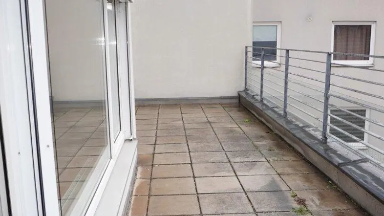 Große Dachterrasse mit Betonplatten und Metallgeländer, umgeben von Gebäudefassaden.