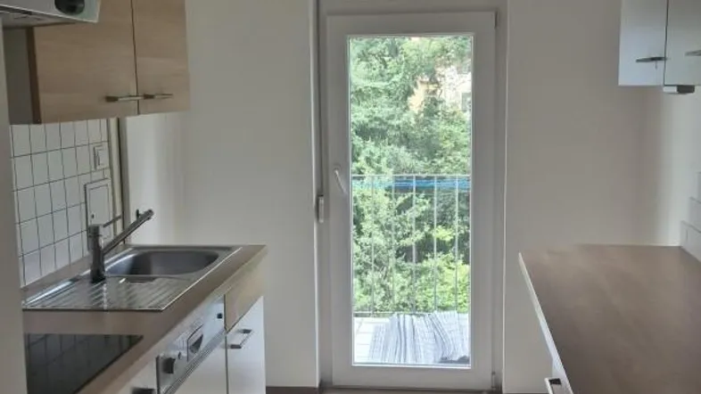 Helle Küche mit Holzarbeitsplatte, Einbauschränken und Zugang zu einem Balkon mit Grünblick.