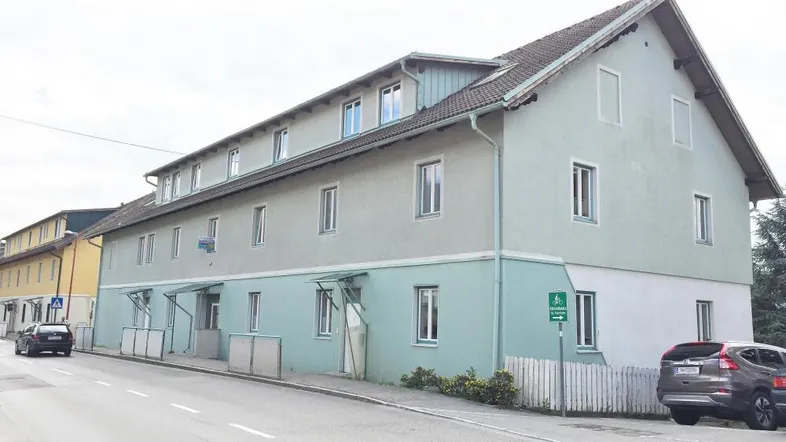 Mehrfamilienhaus mit hellgrüner Fassade und Satteldach an einer ruhigen Straße gelegen.
