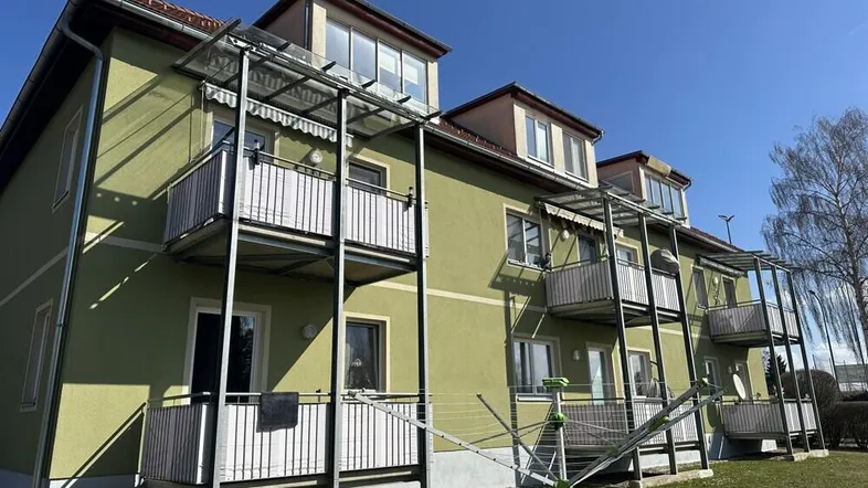 Mehrfamilienhaus mit grüner Fassade, mehreren Balkonen und Wäscheleine im Vorgarten.