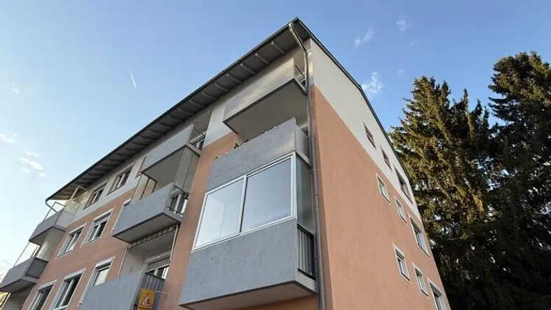Mehrstöckiges Wohngebäude mit Balkonen und einer Fassade in Pastellfarben unter blauem Himmel.