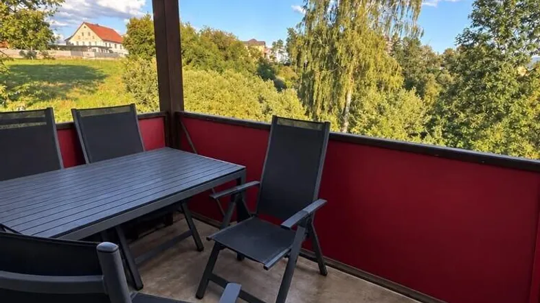 Gemütlicher Balkon mit Esstisch und Stühlen, umgeben von grüner Landschaft und Fernblick.