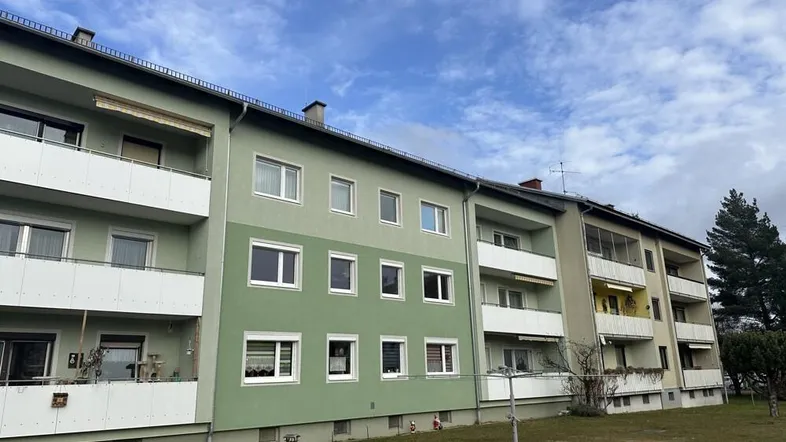 Mehrfamilienhaus mit Balkonen und grüner Fassade unter bewölktem Himmel.