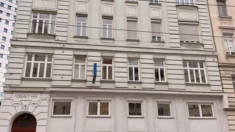 Klassisches Mehrfamilienhaus mit historischer Fassade, vielen Fenstern und parkenden Autos davor auf der Straße.