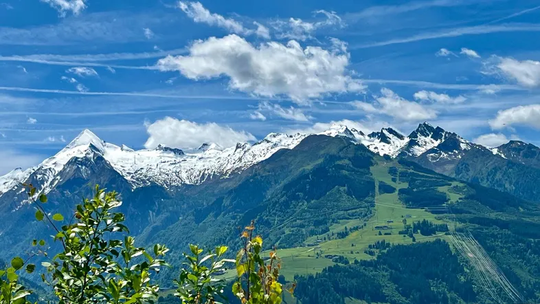 Panoramablick auf schneebedeckte Berge und grüne Täler unter einem strahlend blauen Himmel.