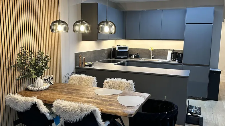 Moderne offene Küche mit grauen Schränken, Holztisch und dekorativer Holzlamellenwand im Essbereich.