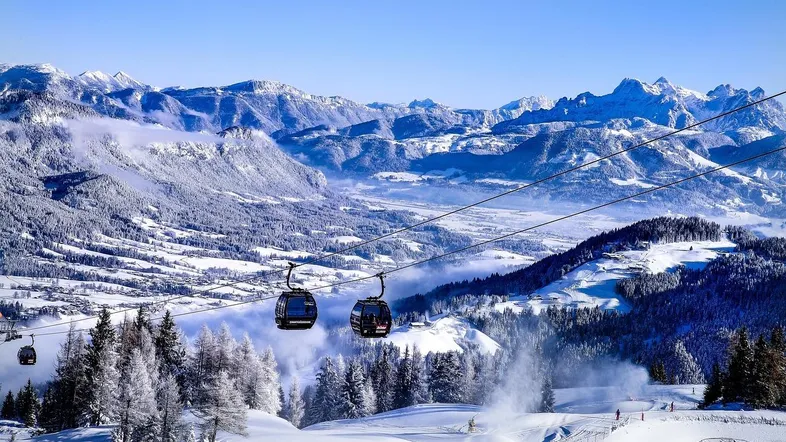 Winterlandschaft mit schneebedeckten Bergen, Gondelbahnen und Skipisten unter blauem Himmel.