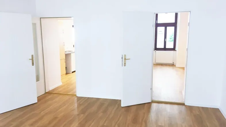 Heller, leerer Raum mit neuem Laminatboden und weißen Wänden, der zu weiteren Zimmern führt.