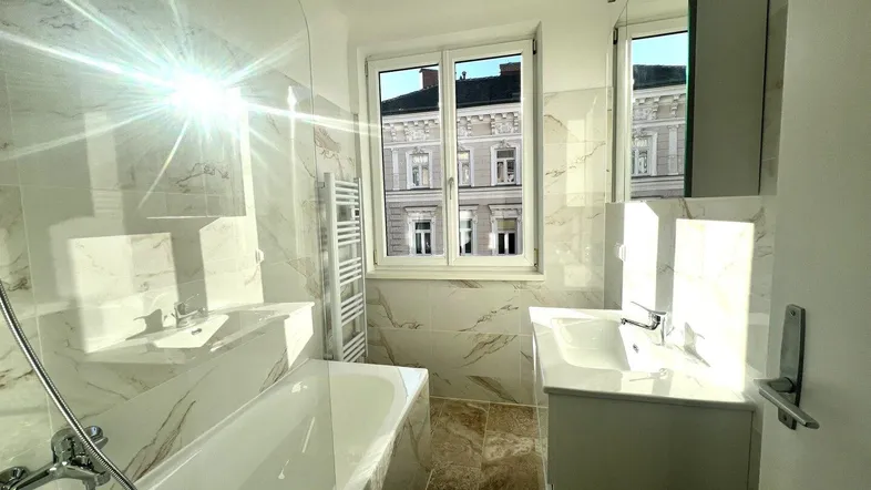 Helles Badezimmer mit Badewanne, modernen Fliesen und Fenster mit Stadtblick.