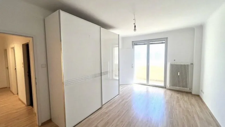 Helles Zimmer mit Laminatboden, weißem Schrank und Zugang zu einem Balkon.