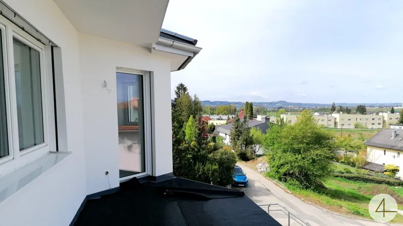 Heller Balkon mit weitem Blick über die grüne Landschaft und angrenzende Wohnsiedlung.