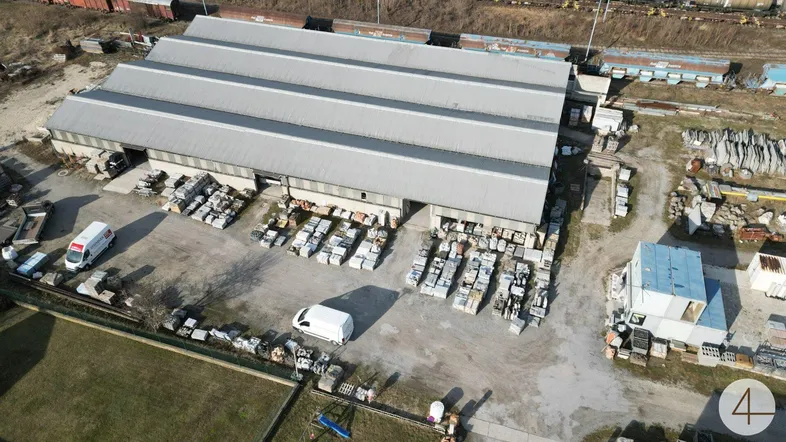 Luftaufnahme eines Industriegebäudes mit Lagerflächen und angrenzenden Bahngleisen unter klarem Himmel.