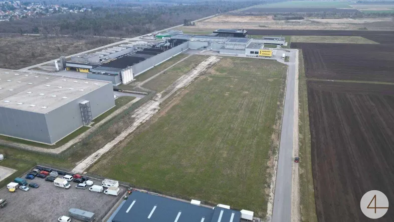 Luftaufnahme eines Gewerbegebiets mit mehreren Hallen, angrenzenden Feldern und Parkplätzen.