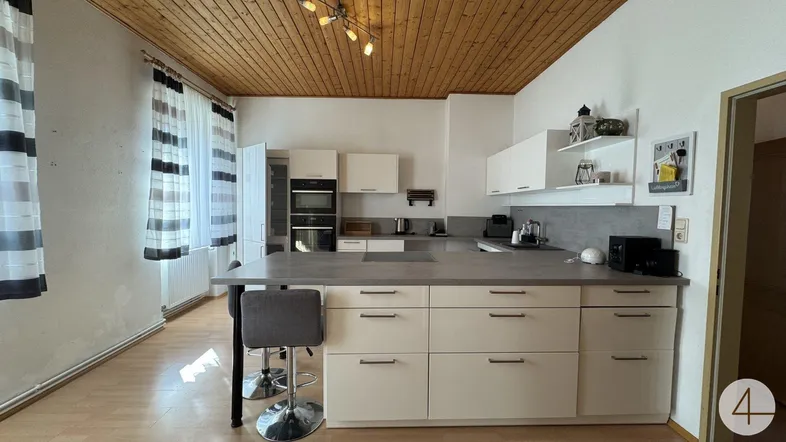 Moderne Küche mit heller Einbauküche, Kochinsel und Holzdeckenverkleidung.