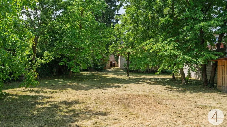 Großer Gartenbereich mit Rasenfläche, Bäumen und einem kleinen Holzschuppen im Hintergrund.