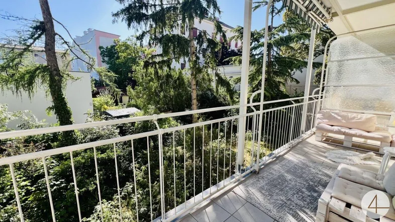 Heller Balkon mit weißem Geländer, gemütlichen Sitzgelegenheiten und Blick ins Grüne.